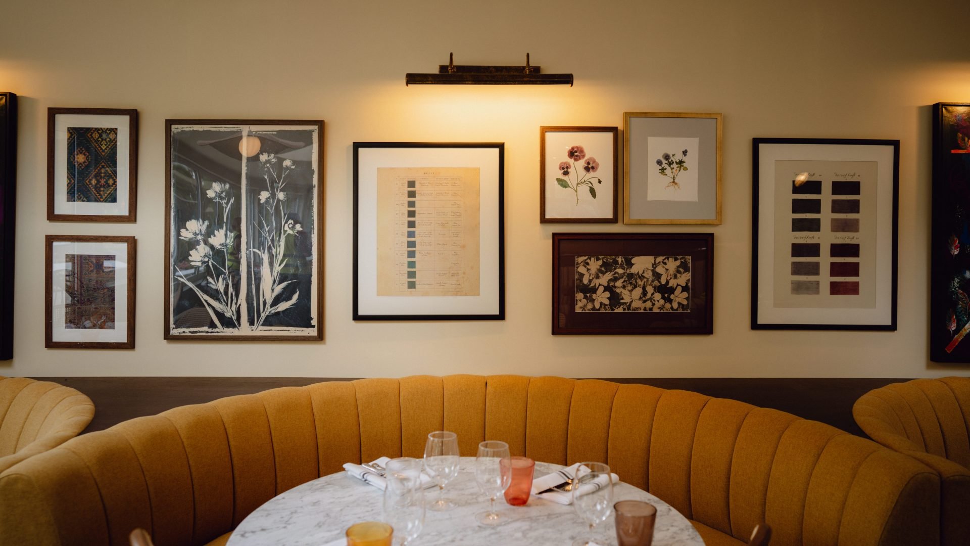 A dining table and chairs in front of a selection of wall hung paintings